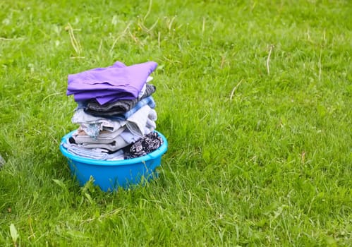 Colorful washed dry clothes in plastic bowl on the green grass background.