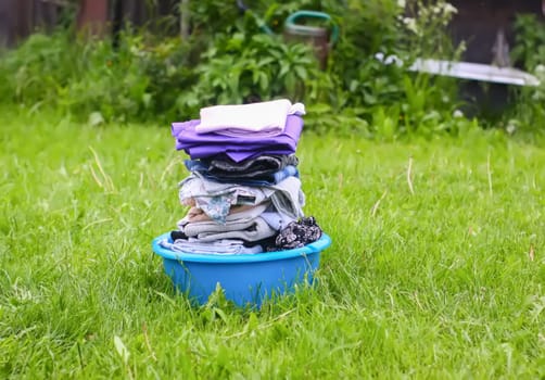 Colorful washed dry clothes in plastic bowl on the green grass background.