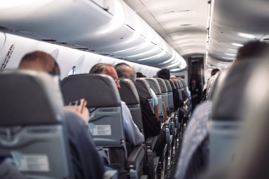 Interior of airplane with passengers on seats and stewardess in uniform walking the aisle, serving people. Commercial economy flight service concept