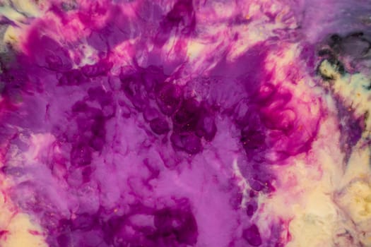 A close up of purple and yellow ink swirling in water, creating a vibrant art piece reminiscent of petals on a violet or magenta plant