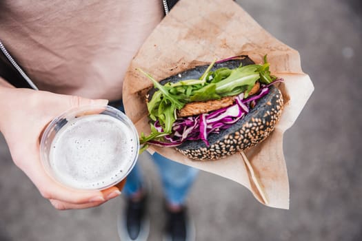 Close up of woman hands holding delicious organic salmon vegetarian burger and homebrewed IPA beer on open air beer an burger urban street food festival in Ljubljana, Slovenia