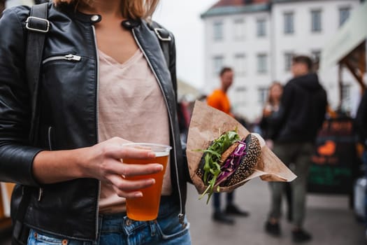 Close up of woman hands holding delicious organic salmon vegetarian burger and homebrewed IPA beer on open air beer an burger urban street food festival in Ljubljana, Slovenia