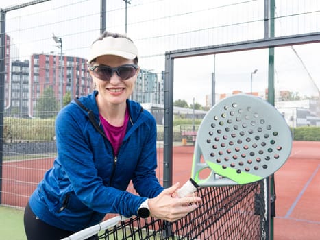 Portrait of positive young woman with racket and padel ball on tennis court. High quality photo