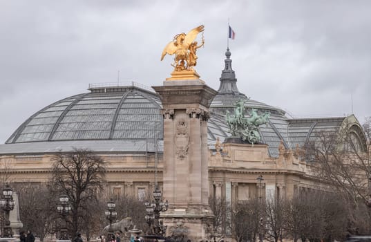 France, Paris - Jan 04, 2024 - View of The magnificent golden statue at Pont Alexandre III bridge with The Grand Palais des Champs-Elysee in background. This building with Large exhibition hall and museum center in Beaux-Arts architecture style was built made of glass, iron, steel and concrete. Space for text, Selective focus.