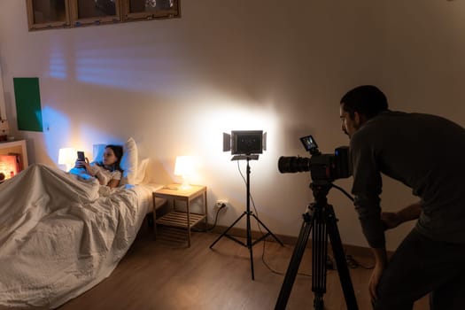 Film bedroom set with attractive model in the bed and camera operator with lights. Behind the scenes. High quality photo