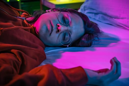 Top view of a beautiful girl sleeping cozily on a bed in her night room with colorful neon lights. High quality photo