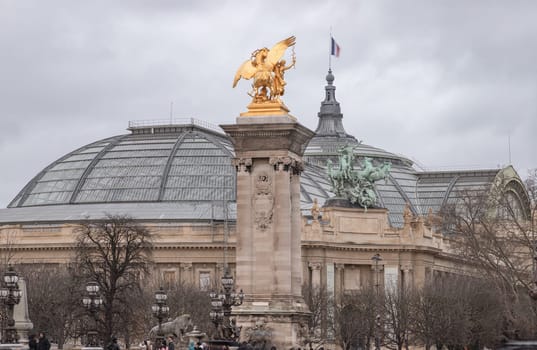 France, Paris - Jan 04, 2024 - View of The magnificent golden statue at Pont Alexandre III bridge with The Grand Palais des Champs-Elysee in background. This building with Large exhibition hall and museum center in Beaux-Arts architecture style was built made of glass, iron, steel and concrete. Space for text, Selective focus.