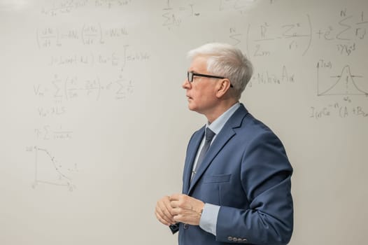 Mature man stands at a white board with written formulas