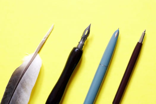 The development of the fountain pen. Set of various pens closeup on yellow paper background