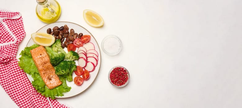 Healthy lunch with grilled salmon on green lettuce, next to vegetables, tomatoes, radishes, broccoli and a portion of beans. Copy space