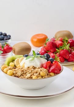 Granola with strawberries, kiwi, banana and blueberries in a round plate topped with yogurt on the table. Healthy and tasty food