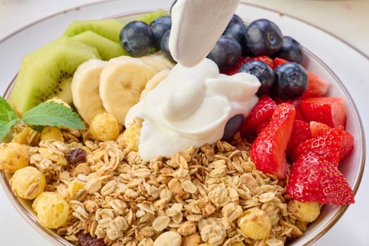 Granola with strawberries, kiwi, banana and blueberries in a round plate topped with yogurt on the table. Healthy and tasty food, top view