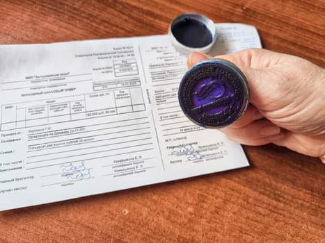 Kirov, Russia - March 18, 2024: Close-up of hand pressing a seal onto paper. Woman Applying Seal to Official Document on Table