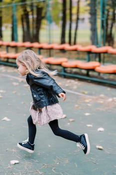 Little girl runs past rows of seats on a sports ground. Side view. High quality photo