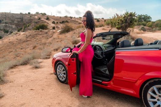 A woman in a red dress stands in front of a red convertible. The scene is set in a desert, with the woman posing for a photo. Scene is playful and fun, as the woman is dressed up