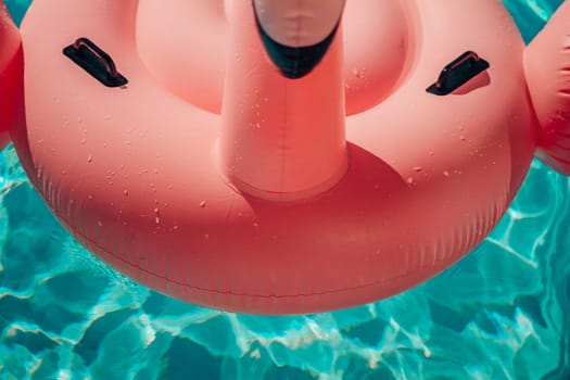 A pink inflatable flamingo is floating in a pool. The water is clear and calm. The flamingo is the main focus of the image, and it is enjoying its time in the water