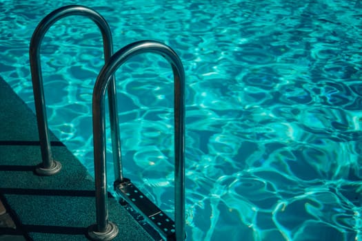 A metal ladder is in the water. The water is clear and calm. The ladder is in the middle of the pool