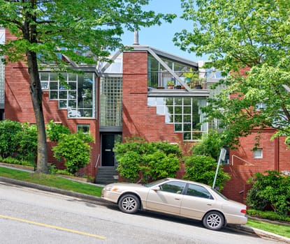 A perfect nighbourhood. Residential townhouses on the street going uphill with a car parked in front.