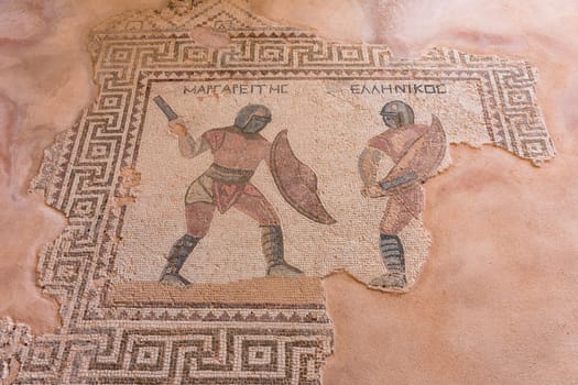 A mosaic of two men fighting with swords. The men are wearing red and black. The mosaic is on a brown surface. Κourion ancient ruins, Cyprus.