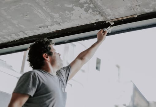 Portrait of a handsome young caucasian brunette man with curly hair smiling broadly looking at the camera and standing near the window opening without glass, close-up side view. The concept of installing windows, construction.