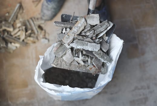 Young caucasian unrecognizable man holding a small construction debris broom on an old dustpan over a full bag on the floor, close-up side view with depth of field. The concept of cleaning and installing windows, construction work, home renovation.