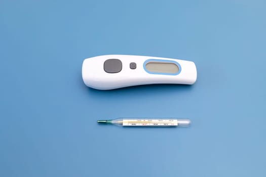 Top View No Touch Thermometer and Glass Oral Mercury Thermometer with Reading Fever Indicator on Blue Background. Digital Accurate Thermometer with Fever Alarm for Adults and Kids. Horizontal Plane.