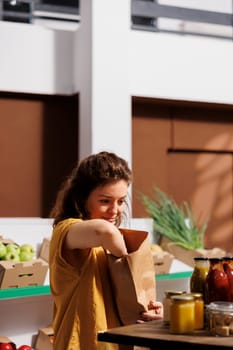 Smiling woman buying bio produce in zero waste store using reusable biodegradable paper bags to minimize plastic usage. Green living customer looking for ethically sourced pantry staples