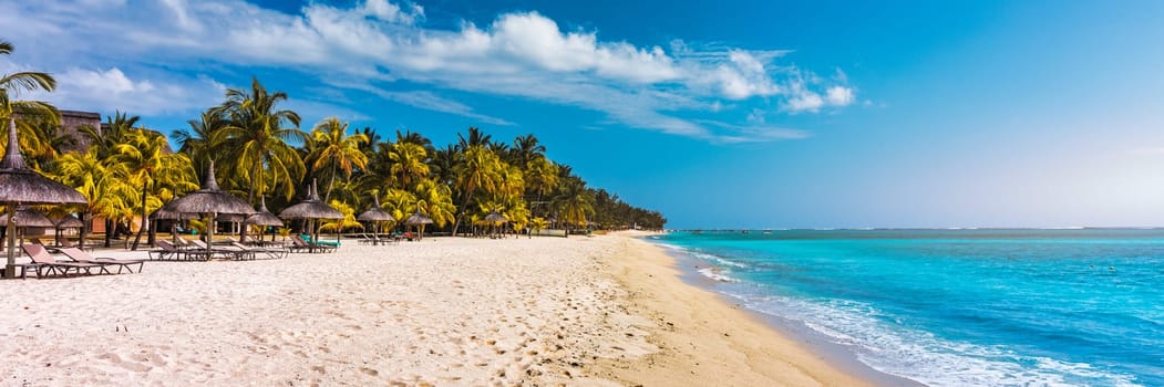 A beach with palm trees and umbrellas on Le morne Brabant beach in Mauriutius. Tropical crystal ocean with Le Morne beach and luxury beach in Mauritius. Le Morne beach with palm trees, white sand and luxury resorts, Mauritius.