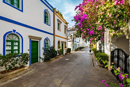 Street with blooming flowers in Puerto de Mogan, Gran Canaria, Spain. Favorite vacation place for tourists and locals on island. Puerto de Mogan with lots of bougainvillea flowers, Canary Island.