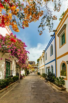 Street with blooming flowers in Puerto de Mogan, Gran Canaria, Spain. Favorite vacation place for tourists and locals on island. Puerto de Mogan with lots of bougainvillea flowers, Canary Island.