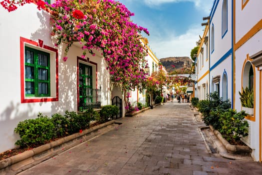 Street with blooming flowers in Puerto de Mogan, Gran Canaria, Spain. Favorite vacation place for tourists and locals on island. Puerto de Mogan with lots of bougainvillea flowers, Canary Island.