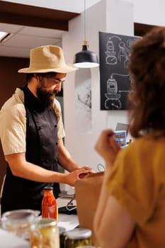 Merchant in zero waste shop at checkout counter bagging customer order. Customer buying organic food from her ecofriendly local neighborhood store with no plastic bags policy