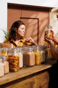 Man and woman in zero waste store filling shopping baskets with healthy locally sourced bulk products. Environmentally responsible clients buying pantry staples from local neighborhood shop