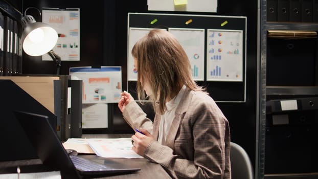 In criminal investigation office, dedicated caucasian policewoman examines evidence with personal computer. Laptop, files, and meticulous investigation all help in the hunt for clues and statements.