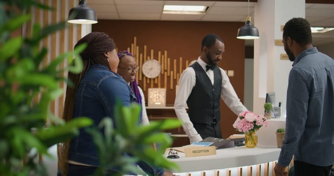 Receptionist doing check in for guests, helping travellers to relax after long flight and see accommodation. Young couple receiving luxurious concierge service at five star holiday retreat.