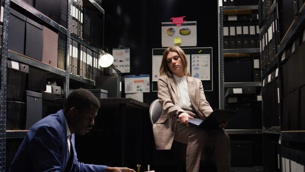 In incident room, multiethnic team of weary private investigators analyzes evidence, reviews files, and does research to solve the case. Two detectives are exhausted by criminal investigation reports.