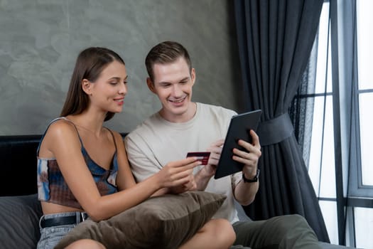 Young couple sit in the home bedroom using online payment app and digital wallet on smartphone to pay with credit card. E commerce shopping and modern purchasing via mobile internet. Unveiling