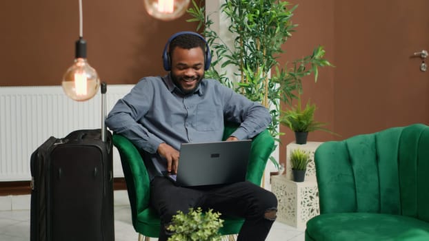 Hotel guest enjoys tv movie in lobby at holiday retreat, waiting for check in procedure and killing time with film on laptop. Modern person using pc in lounge area after long flight.