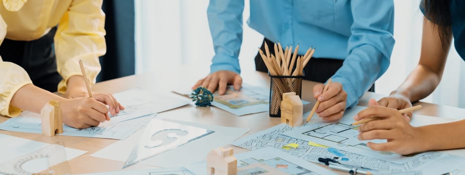 A portrait of professional architect team discussion about architectural project on meeting table with blueprint and wooden block scatter around at modern office. Closeup. Focus hand. Delineation.