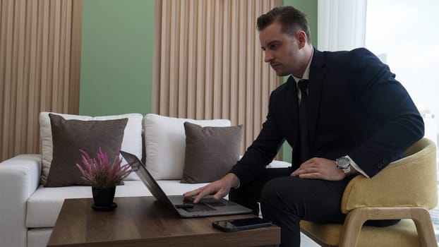 Businessman sitting on furniture working on laptop at ornamented corporate waiting area for meeting preparation. Office worker or business profession and strategic marketing plan for business success.