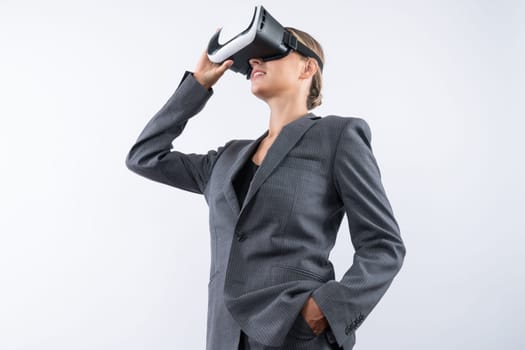 Skilled businesswoman looking at visual reality world by using VR glass while standing at background. Smart manager holding VR goggle to connect metaverse by using technology innovation. Contraption.