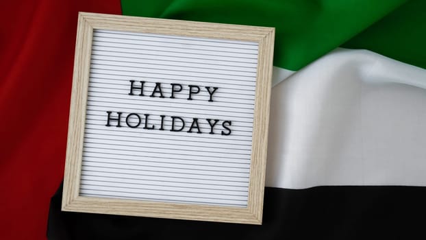 Text HAPPY HOLIDAYS on background waving flag of UAE. Independence Commemoration Day Muslim, Ramadan, Day of flag National holiday of United Arab Emirates. Arabian holidays. Dubai celebration