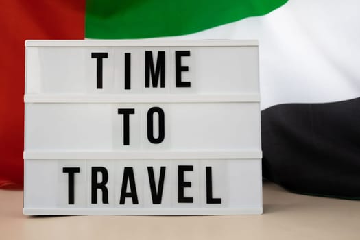 Message with text TIME TO TRAVEL on background of waving UAE flag made from silk. United Arab Emirates flag with concept of tourism and traveling. Inviting greeting card, advertisement. Dubai welcoming card