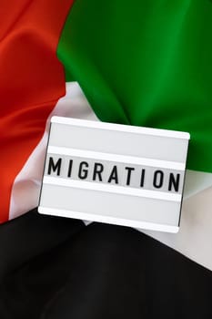 Lightbox with text MIGRATION on background of waving UAE flag made from silk. United Arab Emirates flag with concept of tourism and traveling. Inviting greeting card, advertisement. Dubai welcoming card