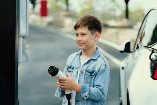 Little boy recharging eco-friendly electric car from EV charging station. EV car road trip travel concept for alternative transportation powered by clean renewable and sustainable energy. Perpetual