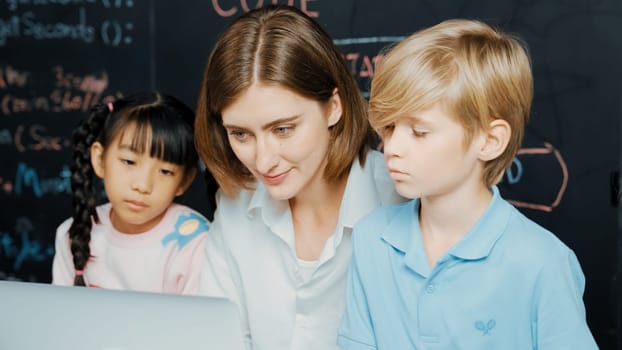Young smart teacher using laptop to teach diverse student programing system. Caucasian learner looking at computer screen while study about coding prompt at blackboard with program code. Erudition.
