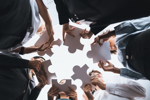 Below view of diverse corporate officer workers collaborate in office connecting puzzle pieces as partnership and teamwork concept. Unity and synergy in business idea by merging jigsaw puzzle. Concord