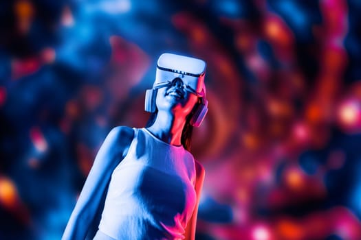 Smart female standing surrounded by neon light wearing VR headset connecting metaverse, future cyberspace community technology. Elegant woman looking faraway and smiling satisfactorily. Hallucination.