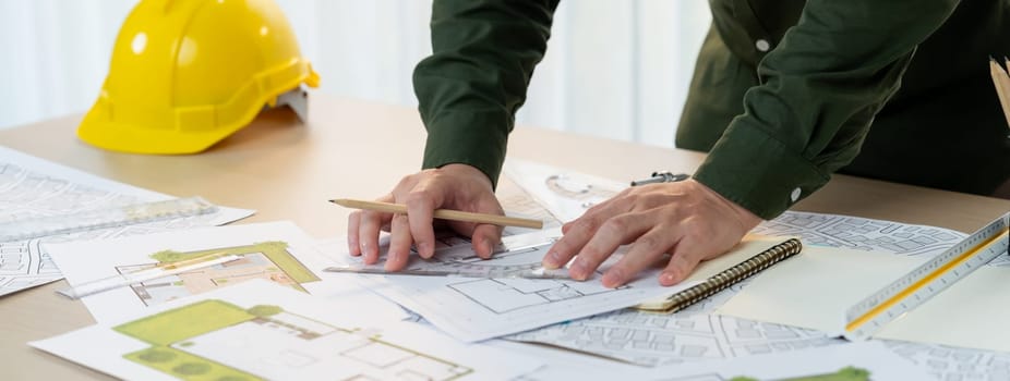 Professional engineer measuring the blueprint. Professional engineer working architectural project at studio on a table with yellow helmet and architectural equipment scatter around. Delineation.