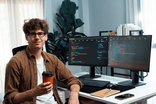 IT developer in online software development looking at camera and holding coffee cup surrounded coding pc screens, working on design new programing for latest version at modern home office. Gusher.